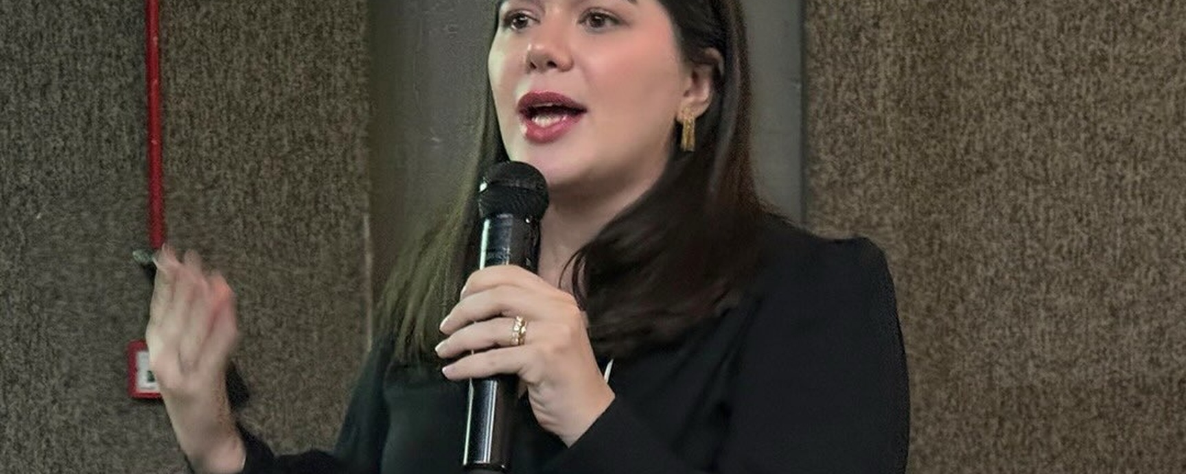 Dra. Débora Eulálio com microfone em um evento de dermatologia.